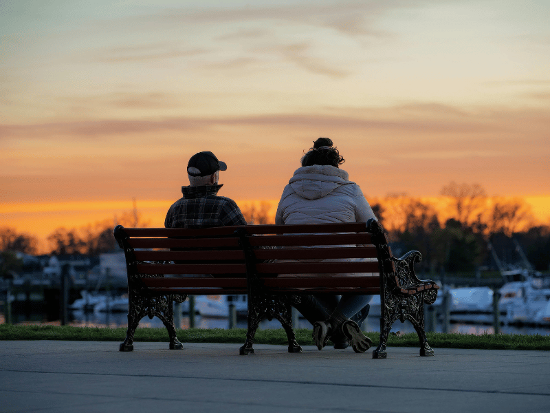 a picture of a man and a woman sat on a bench looking out over a river